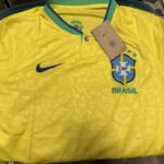 Camisas de futebol, álbuns de figurinhas e produtos da Copa do Mundo 2026 expostos em lojas e centros comerciais brasileiros, destacando a diferença entre itens oficiais e produtos falsificados encontrados no comércio popular.